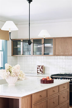 a kitchen with wooden cabinets and marble counter tops, white flowers in a vase on the island