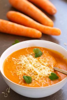 a bowl of carrot soup with parmesan cheese on top and three carrots in the background