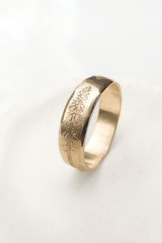 a gold wedding ring with trees engraved on the side, sitting on a white surface