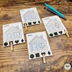 four houses cut out with clothes pins on a wooden table next to a pen and marker