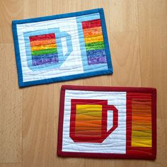 two quilted coasters with colorful designs on them sitting on a wooden floor next to each other