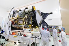 three men in white lab coats standing next to a large space station with an object on it