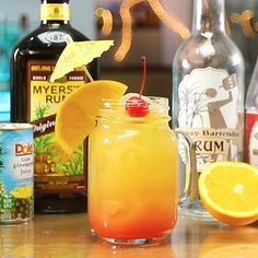 an orange drink in a mason jar surrounded by liquor bottles and lemon wedges on the counter