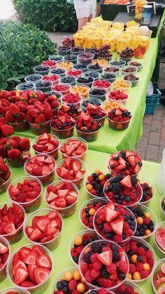 many bowls of strawberries and oranges are on the table with people standing behind them