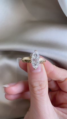 a woman's hand holding an engagement ring with a diamond in the middle, on a white satin background