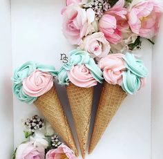 three ice cream cones with pink and blue frosting on them, surrounded by flowers