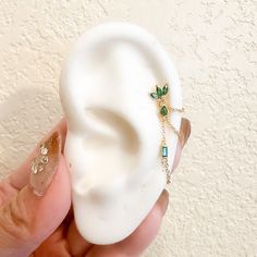 a person is holding a fake ear with green jewels on it and gold chains around the ears