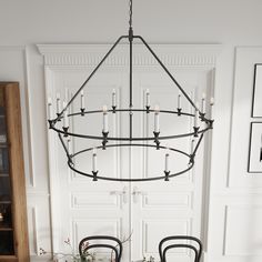 a chandelier hanging over a dining room table with chairs and potted plants