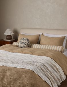 a bed with beige and white comforter in a bedroom next to a night stand