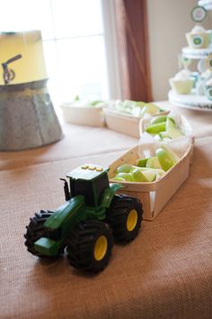 a table topped with boxes filled with apples and a toy tractor next to each other