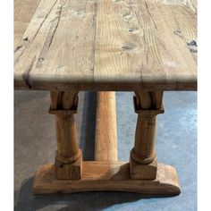 a wooden table with two legs and one leg on the other side, in front of a concrete floor