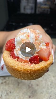 a person holding a pastry with strawberries and whipped cream