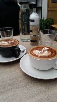 two cups of coffee sitting on top of white saucers next to eachother