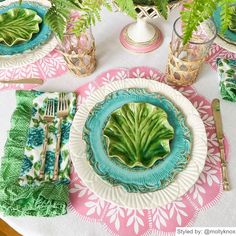 the table is set with plates, silverware and green plants in glass vases