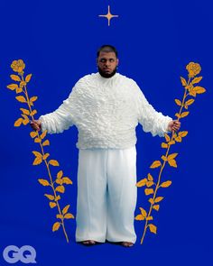 a man standing in front of a blue background wearing white clothing and holding two yellow flowers