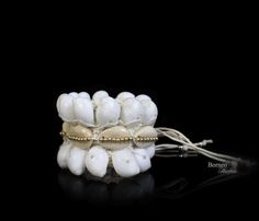 A handwoven white braided rope wide bracelet, decorated with two bands of white curled Shells, a band of cream Cowrie Shells, and a central band of golden round beads. The inner diameter of the bracelet is 2 inches, and the bracelet is 2.1 inches in width. The bracelet is attached by two groups of two, 7.5 inches white cord strands (for adjustable sizing), each decorated at the end with a silver round bead. ► Find these in more dazzling colors here: https://www.etsy.com/listing/231043688/gray-se White Cowrie Shell Beaded Bracelets As Gift, White Cowrie Shell Bracelets As Gift, White Cowrie Shell Bracelet Gift, White Bohemian Beaded Shell Bracelets, White Bohemian Shell Bracelet, White Cowrie Shell Beaded Bracelets, White Cowrie Shell Bracelet, White Shell Friendship Bracelets For Vacation, White Shell Bracelets As A Gift