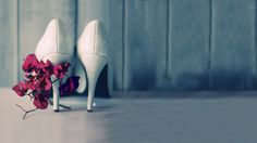 a pair of white high heeled shoes next to a pink flower on the floor