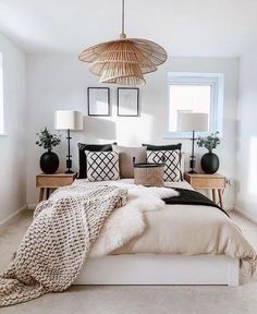 a white bedroom with black and white pillows on the bed, two lamps above the bed