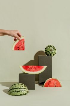 a person holding a slice of watermelon in front of several pieces of fruit