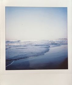 a polaroid photo of the ocean with waves coming in from the shore and sand on the beach