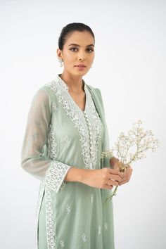 Introducing a charming ensemble featuring a basil green cotton net shirt, delicately hand embroidered and adorned with resham and French knot work. The intricate detailing adds a touch of elegance to the overall design. The shirt is paired with loose-fitting pants in a matching shade, featuring similar resham work on the bottoms, creating a cohesive look. To complete the ensemble, a handworked chiffon dupatta with lace edging is included, providing a graceful finishing touch. Designer Cotton Palazzo Set With Intricate Embroidery, Elegant Straight Lawn Suit For Summer, Elegant Floral Embroidered Sharara For Summer, Elegant Floral Embroidery Sharara For Summer, Elegant Pant Set With Floral Embroidery And Straight Kurta, Summer Wedding Lawn Suit In Pista Green, Green Resham Embroidered Top For Wedding, Elegant Traditional Wear With Dabka Work For Summer, Summer Wedding Pista Green Lawn Suit