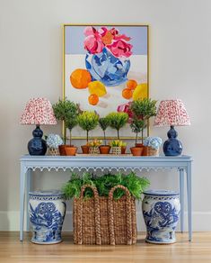 a blue and white table topped with potted plants next to a painting on the wall