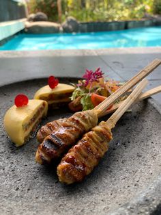 several skewered meats and vegetables on a plate next to a pool