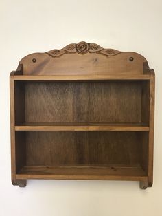 a wooden book shelf with carvings on the top and bottom shelves, against a white wall