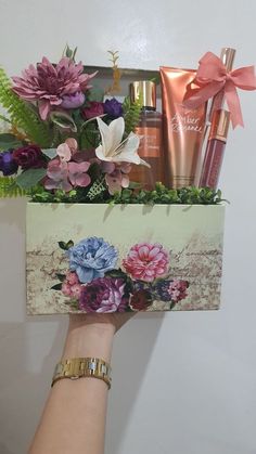 a woman's hand holding a box with flowers and cosmetics