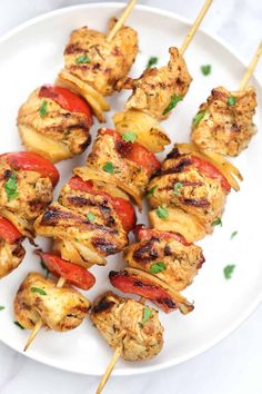 chicken kabobs on skewers with peppers and onions served on a white plate