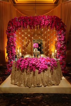 the table is covered with pink flowers and lit candles in front of an elaborate mirror