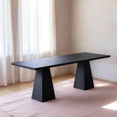 a black table sitting on top of a wooden floor next to a white curtained window