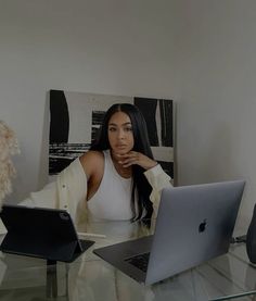 a woman sitting at a glass table with two laptops in front of her and a teddy bear behind her