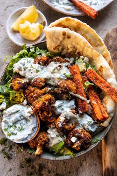 a bowl filled with food next to two plates of pita bread and dipping sauce