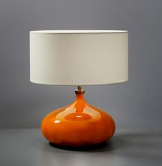 an orange glass table lamp with a white shade on the base and a grey wall behind it