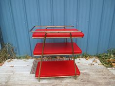 three tiered serving cart with red plastic and gold trimmings on the bottom shelf