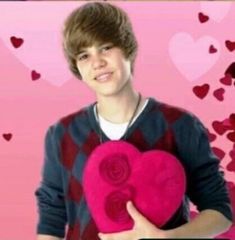 a young man holding a heart shaped pillow in front of a pink background with hearts