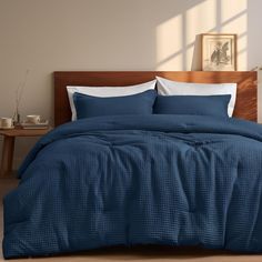 a bed with blue comforter and pillows in a room next to a table on the floor