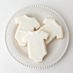 some cookies that are sitting on a plate with white frosting and decorated ones in the shape of baby clothes