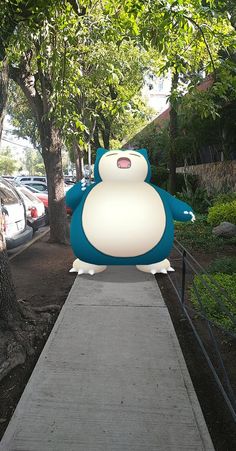 a large blue and white cartoon character sitting on top of a cement walkway next to trees