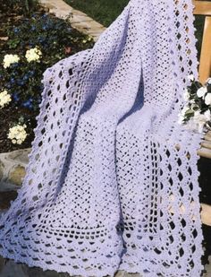 a purple crocheted blanket sitting on top of a wooden bench next to flowers