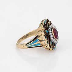 This is part of Chairish’s Fine Jewelry assortment.  Elegant and finely detailed Edwardian era enamel ring (circa 1900s to 1910s), crafted in 14 karat yellow gold.    Created ruby measures 5mm (in very good condition and free of cracks or crisps). Small natural 1mm seed pearls surround the ruby.   A created ruby is set into a beautifully detailed scrolled mount. Blue and black enamel adds a pop of colour, offering contrast to the ruby that is striking and unique. The ring is small in size (2 1/2 Yellow Gold Enamel Jewelry With Rose Cut Diamonds, Vintage Gold Enamel Ring Stamped 14k, Vintage Gemstone Enamel Ring As A Gift, Vintage Enamel Gemstone Ring For Gift, Victorian 14k Gold Ruby Ring With Intricate Design, Ornate Yellow Gold Ruby Ring With Intricate Design, Antique Enamel Ring Collectible, Yellow Gold Enamel Ring With Rose Cut Diamonds, Ornate Yellow Gold Ruby Ring Gift