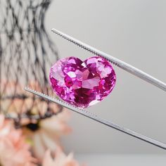 a pink heart shaped diamond being held by two tongs with flowers in the background