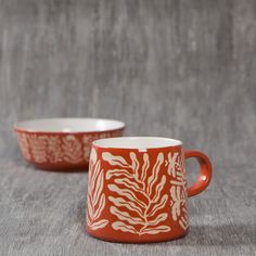 two red and white mugs sitting on top of a gray cloth covered tablecloth