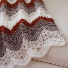 a crocheted blanket sitting on top of a white bed next to a pillow