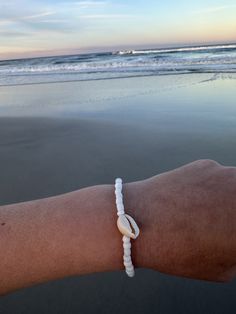 a person's arm with a white bracelet on it and the ocean in the background