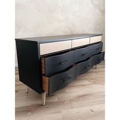 a black and wood dresser with drawers on it's sides, in front of a white wall