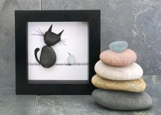 a black cat sitting on top of three rocks next to a small frame with the word love written in it