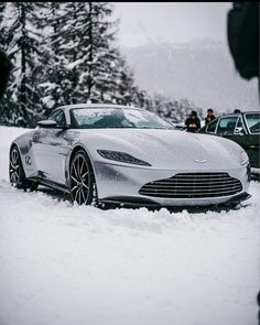 a silver car parked in the snow near other cars and people standing around it on a snowy day