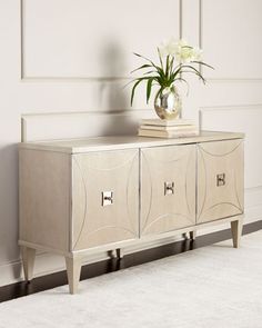 a vase with flowers sitting on top of a silver cabinet next to a white rug